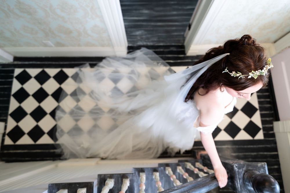 A happy black dog smiles as a bride and groom in wedding attire lean in to kiss it on the cheeks outdoors.