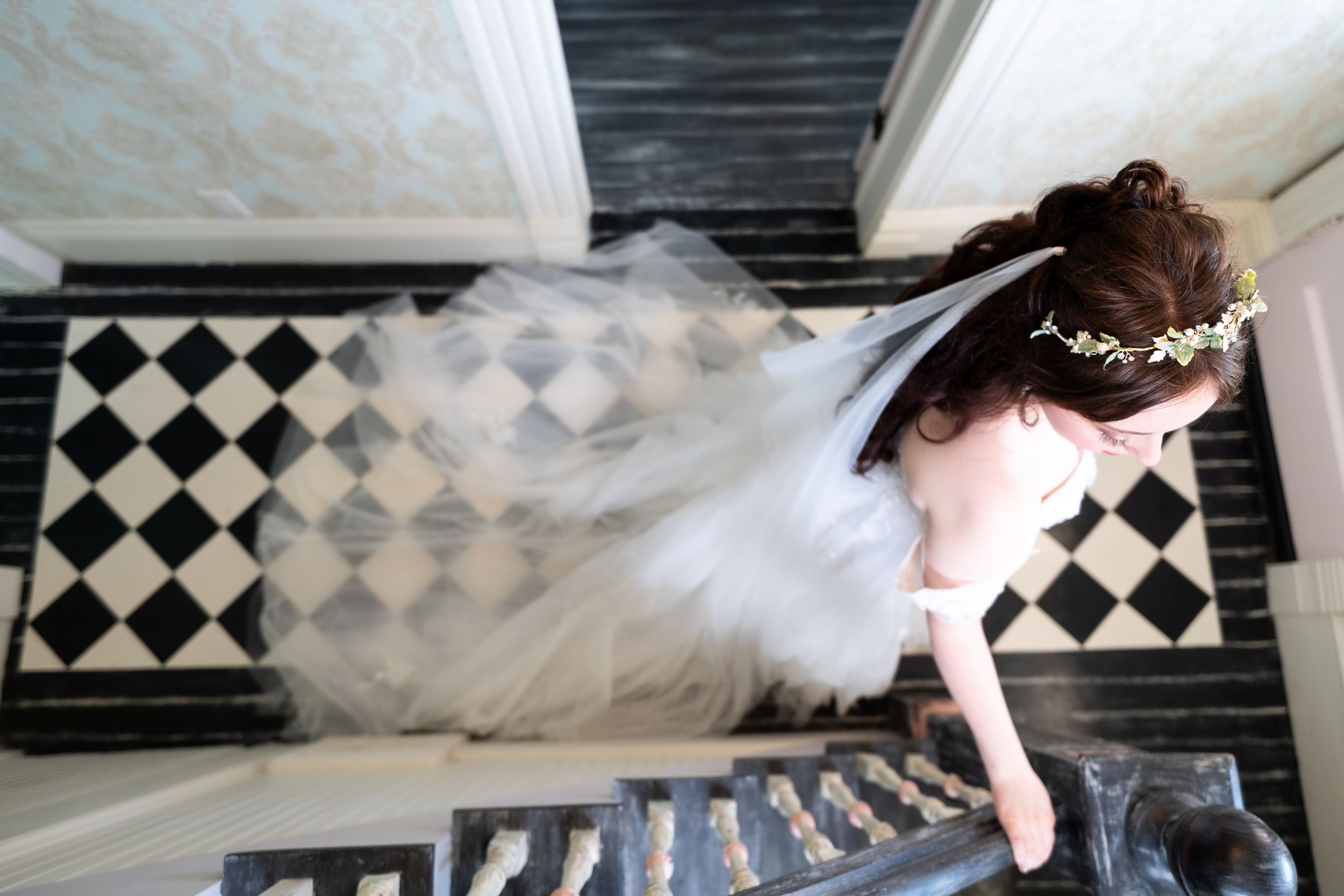 A happy black dog smiles as a bride and groom in wedding attire lean in to kiss it on the cheeks outdoors.