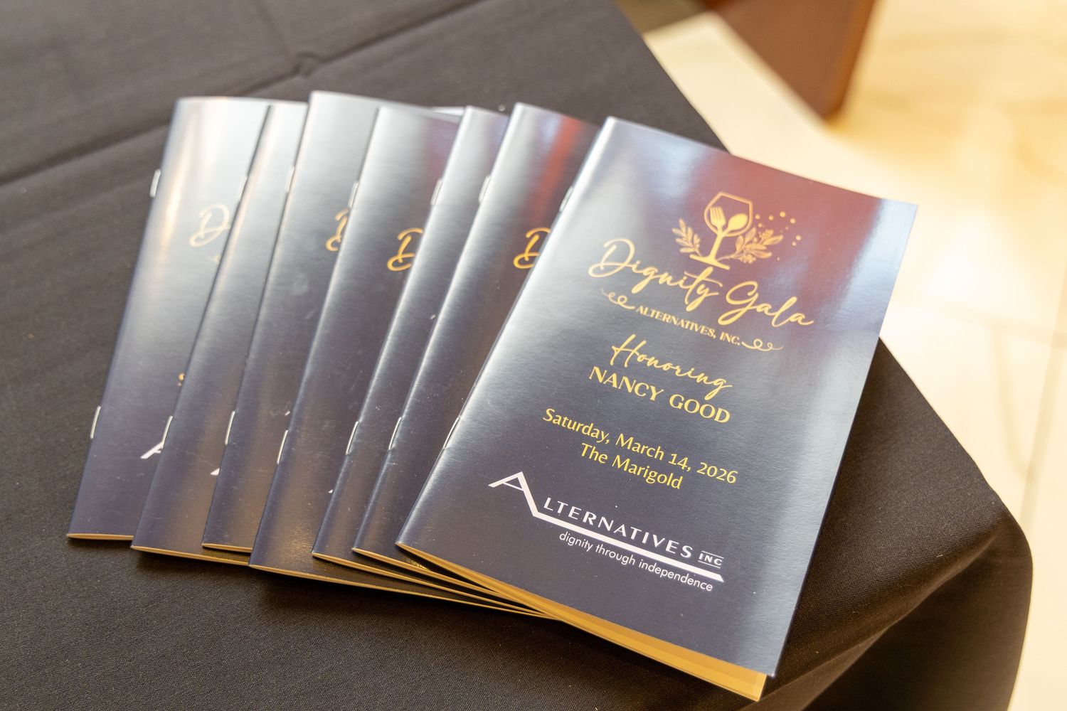 Elegant navy blue and gold event program for Dignity Gala sits beside yellow flowers on white surface.