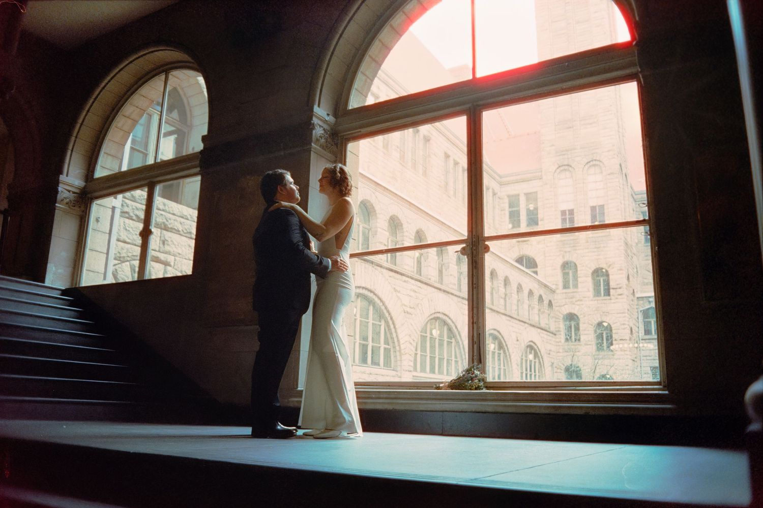 Bride and groom share a moment by arched window in allegheny county courthouse in pgh with halation from being shot on film photography