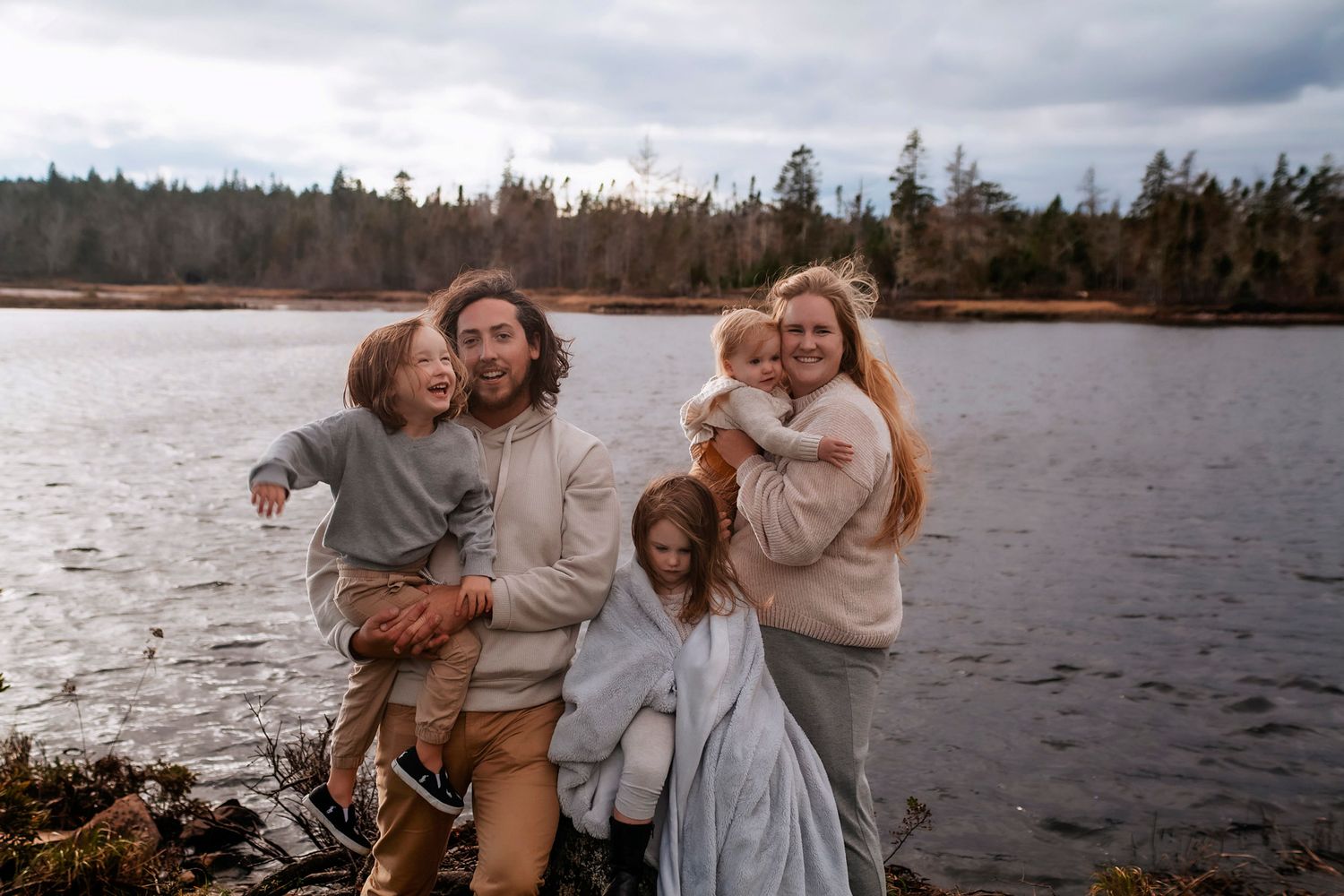at Bridgewater ns Happy family of five smiling together by a scenic lake surrounded by evergreen trees on a cloudy day.