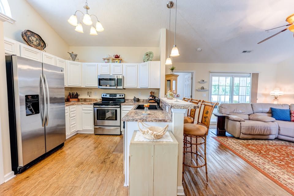 Open-concept kitchen with stainless steel appliances, white cabinets, granite island, and hardwood floors flowing into living area.
