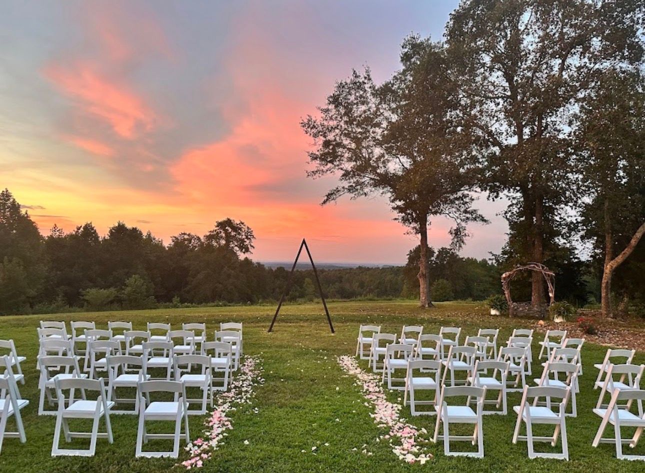 White wedding chairs arranged in rows on a lawn during sunset with vibrant orange and pink sky.