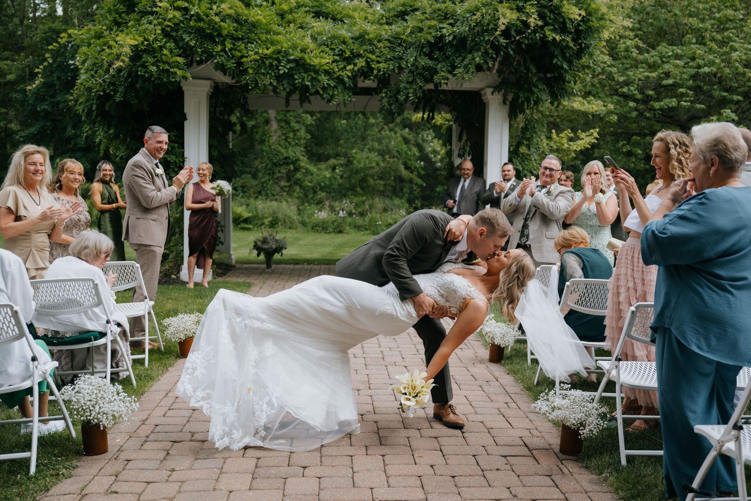 Wedding guests celebrate during an outdoor garden ceremony with white chairs and lush greenery.