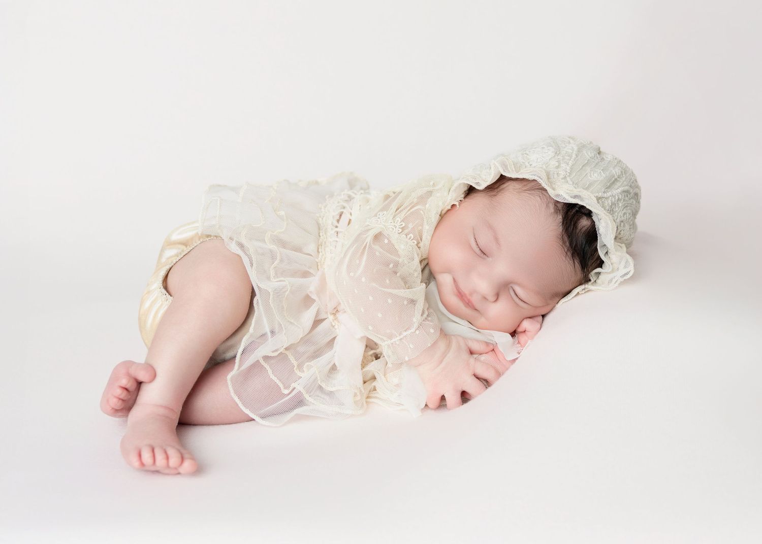 Newborn baby in pink fuzzy outfit sleeping in heart-shaped bowl surrounded by flowers.