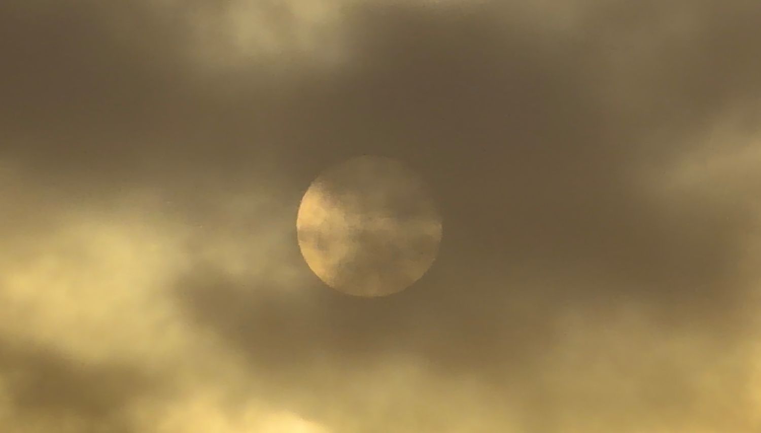Full moon glowing through dramatic golden storm clouds in a moody overcast sky.