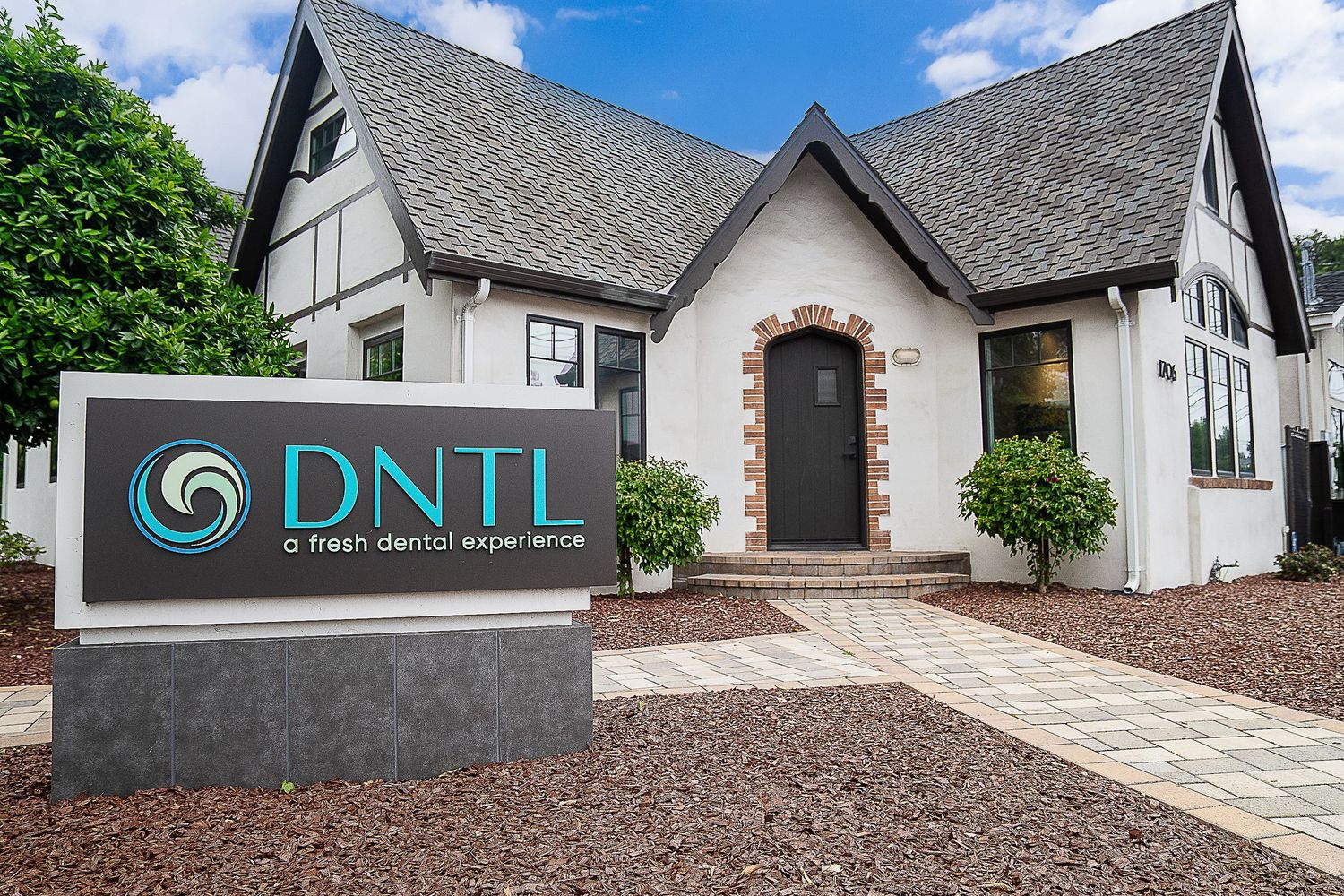 DNTL fresh dental experience office exterior, modern Tudor-style building with dark roof and arched entrance in suburban setting.