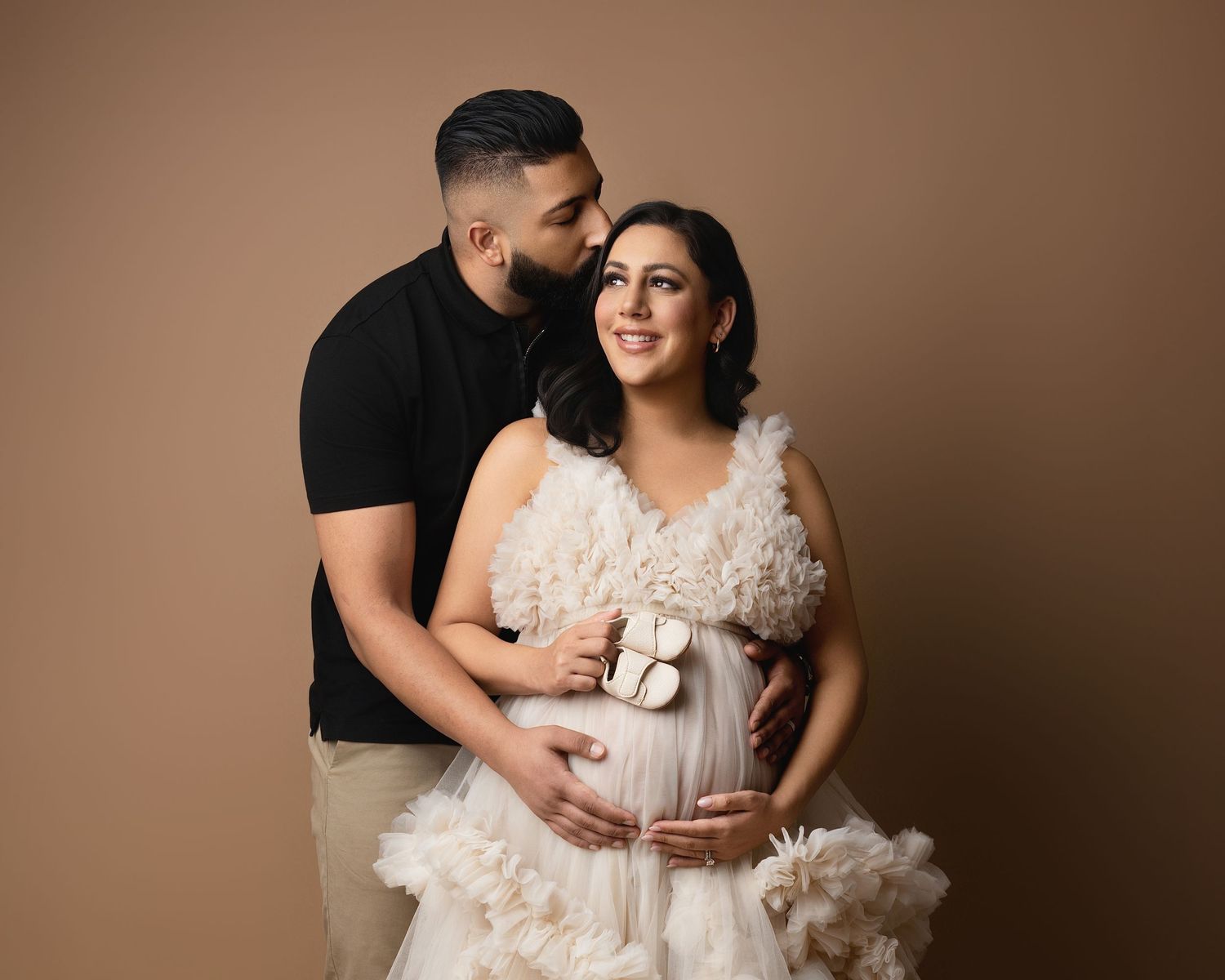 Black and white maternity photo of a couple, man kissing woman's head while cradling her pregnant belly.
