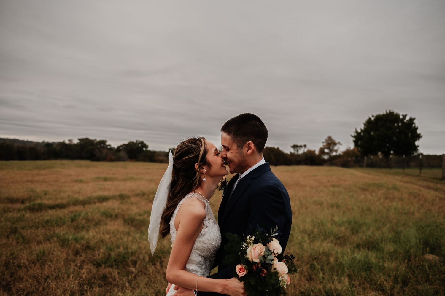 Bride and groom exchange vows at rustic indoor wedding ceremony with white chairs and floral arrangements.