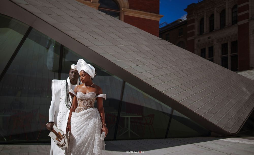 Elegant couple in traditional African wedding attire posing outside a modern geometric building on their wedding day.