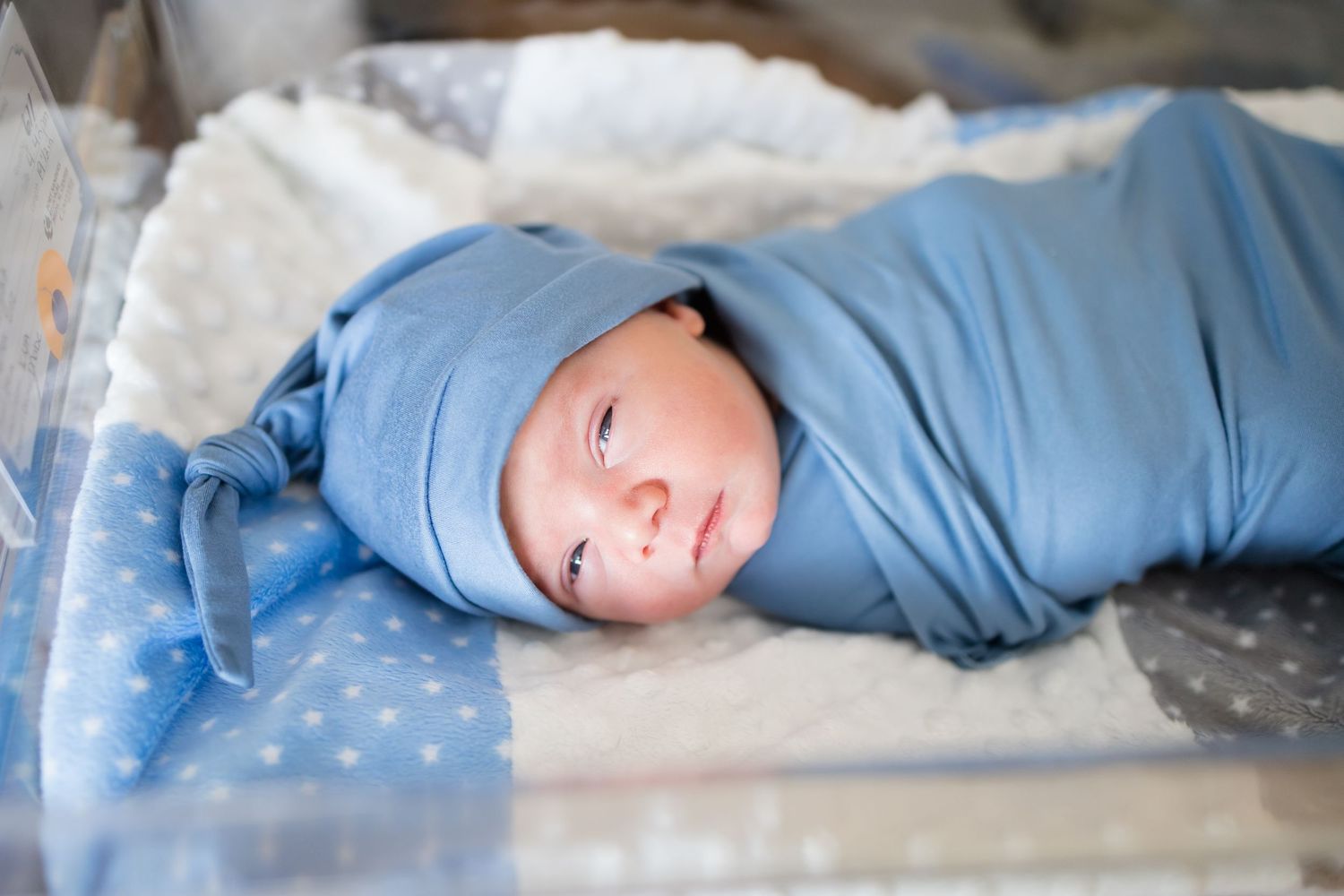 Newborn baby swaddled in a blue wrap and hat lying in a hospital bassinet during a Fresh 48 Session at Fort Sanders in Knoxville, TN.