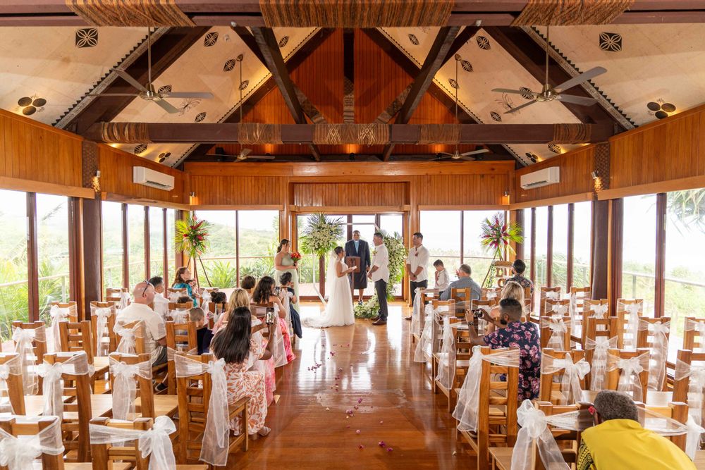 Light-filled wedding ceremony venue with wooden beams and rows of chairs leading to an altar space.