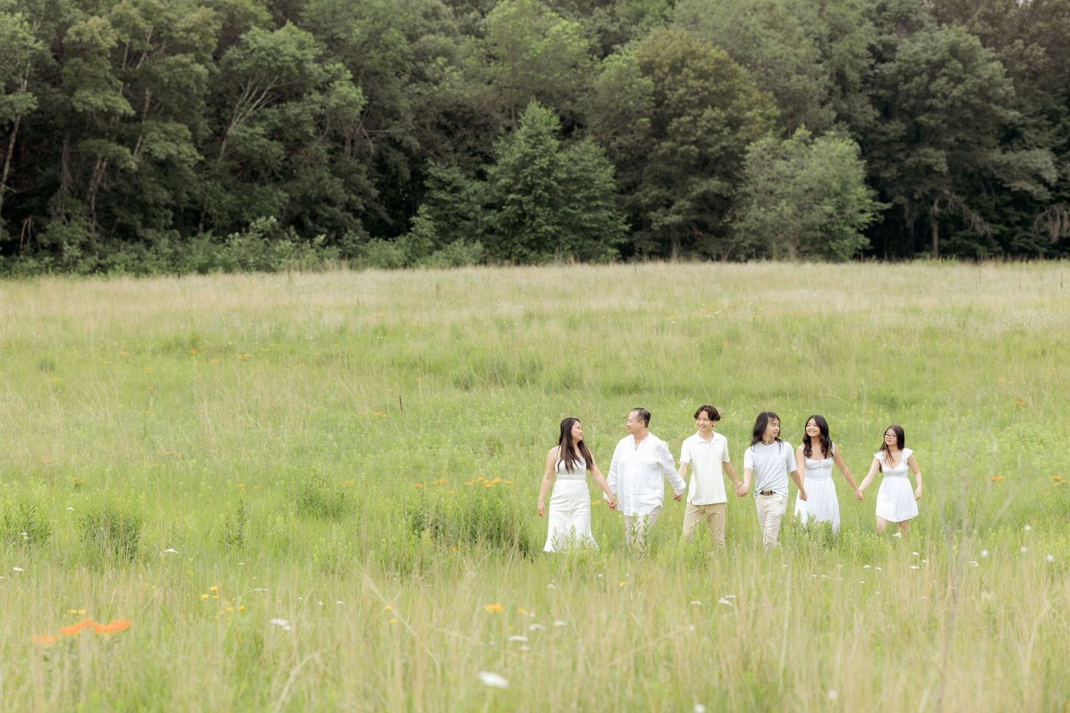 Group in white attire walking through a sunny meadow with wildflowers.