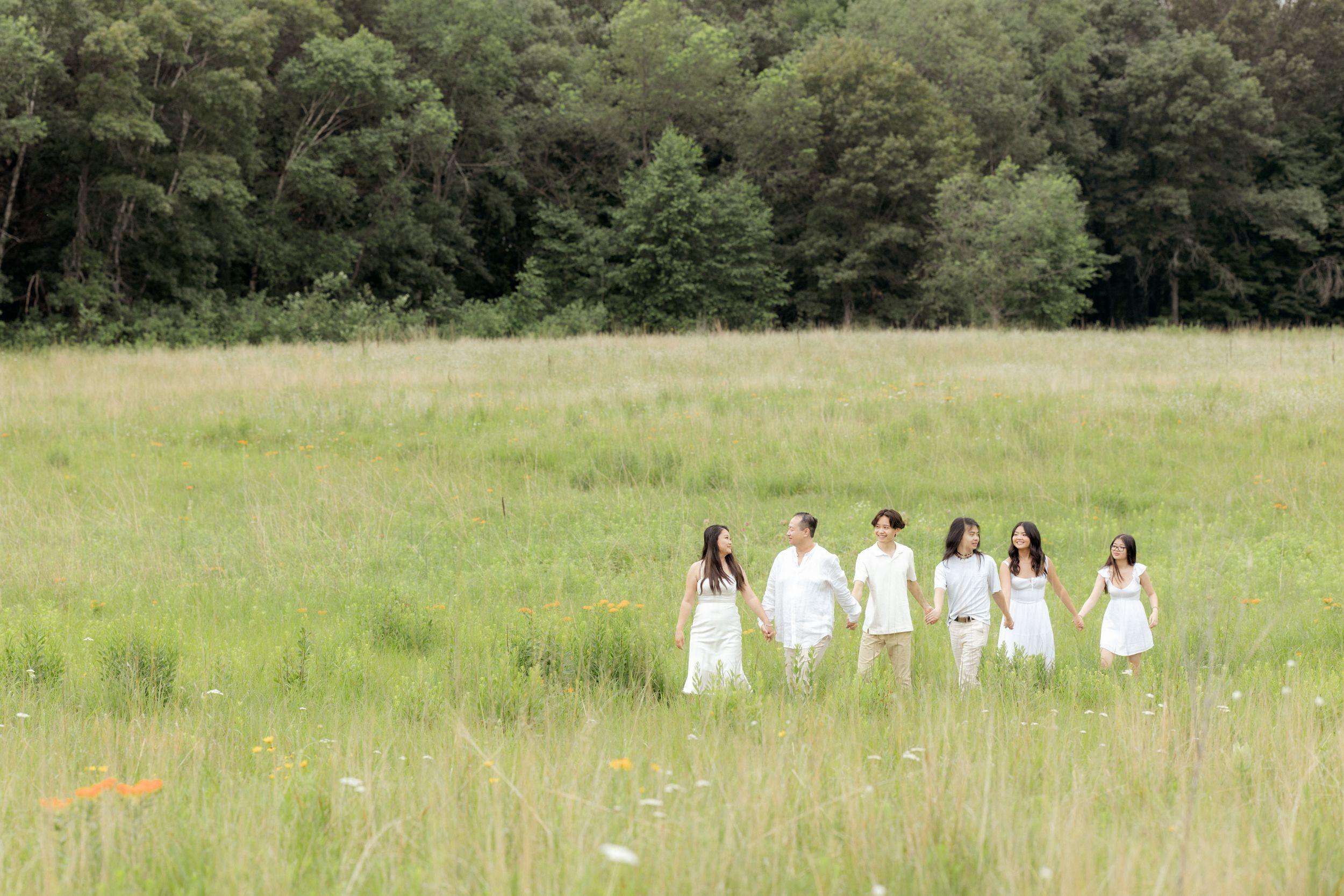 Group in white attire walking through a sunny meadow with wildflowers.