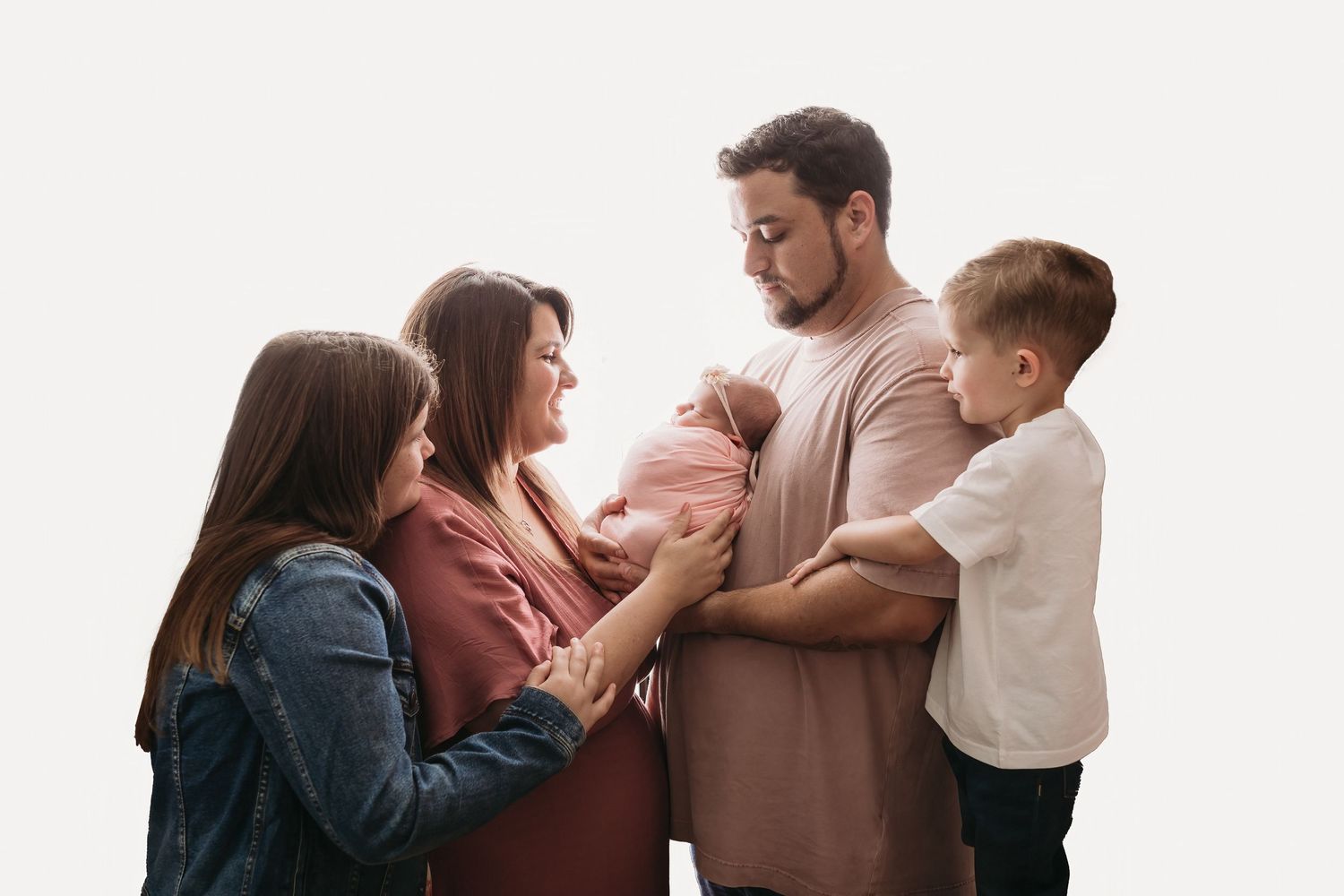 A family group stands together against a white background while admiring a newborn baby.