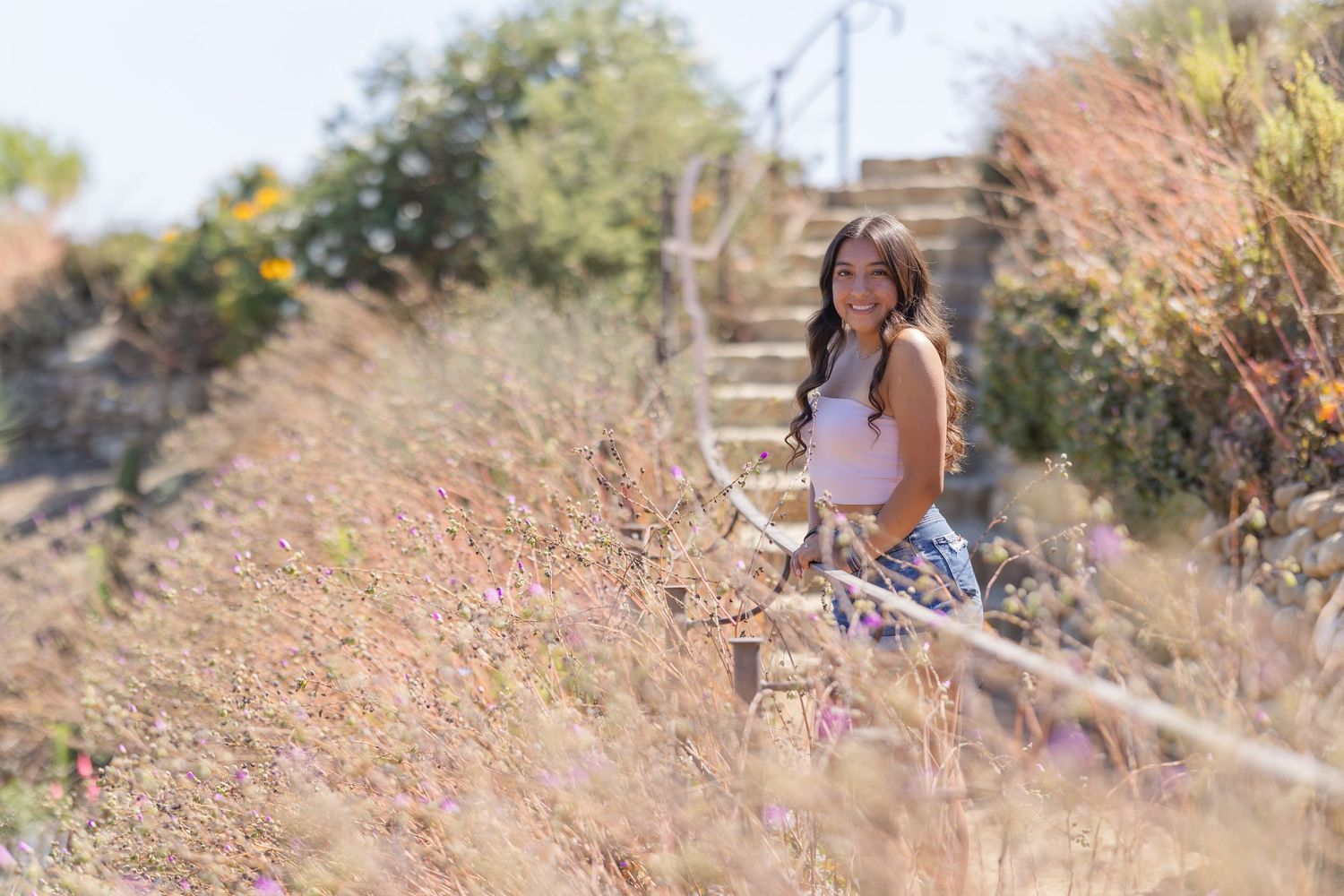Casual portrait on outdoor steps surrounded by wildflowers and natural scenery.