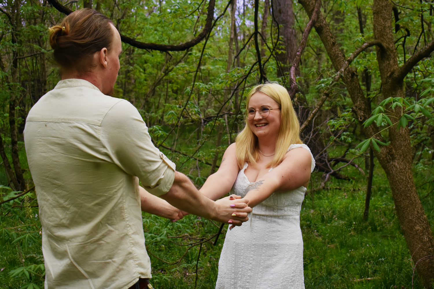 A couple dancing together surrounded by lush green forest trees on a spring day.
