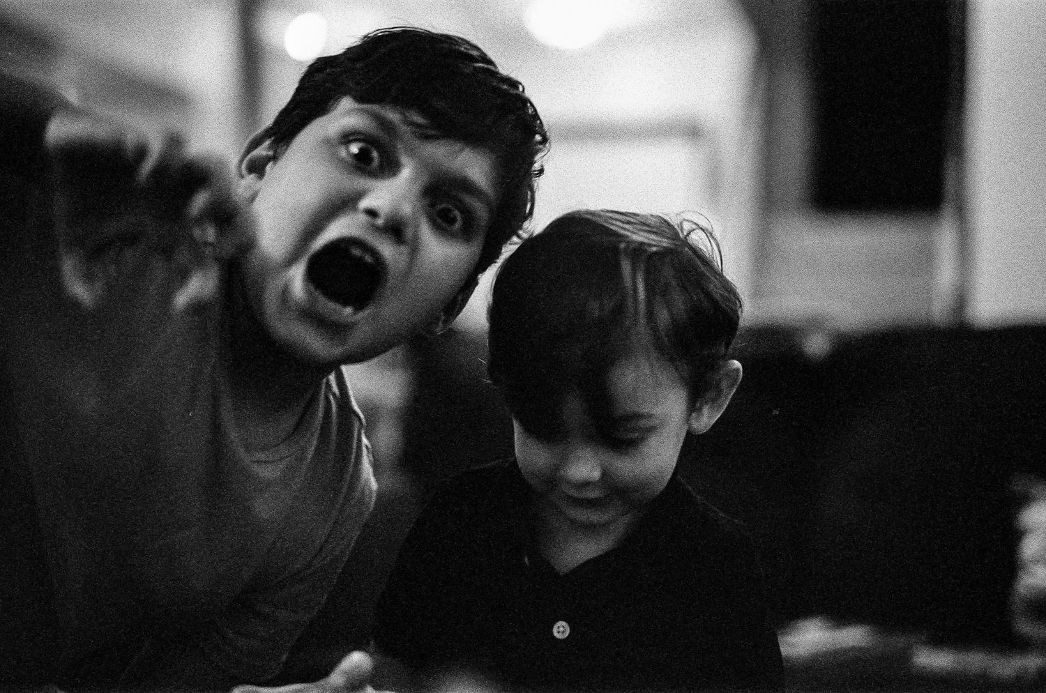 Black and white candid photo showing two children making silly expressions and laughing together.