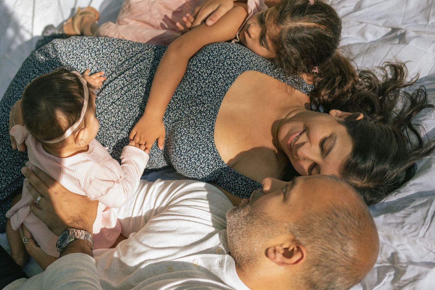 A couple relaxing on white bedding with a young child rests together in an intimate family moment.