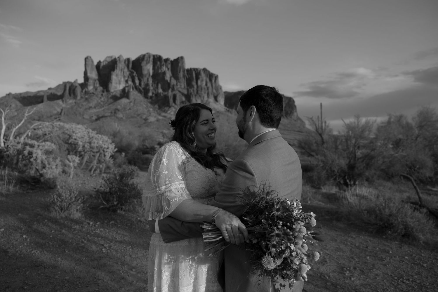 A small outdoor wedding ceremony takes place in front of scenic desert mountains and saguaro cacti in Arizona.