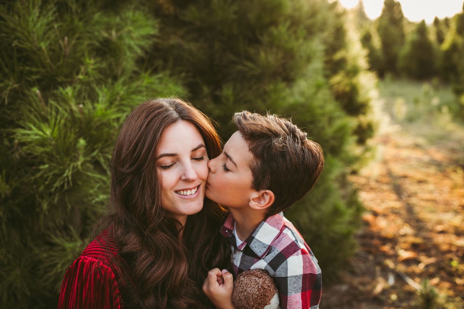 Two people share a tender moment among evergreen trees at a Christmas tree farm during golden hour.