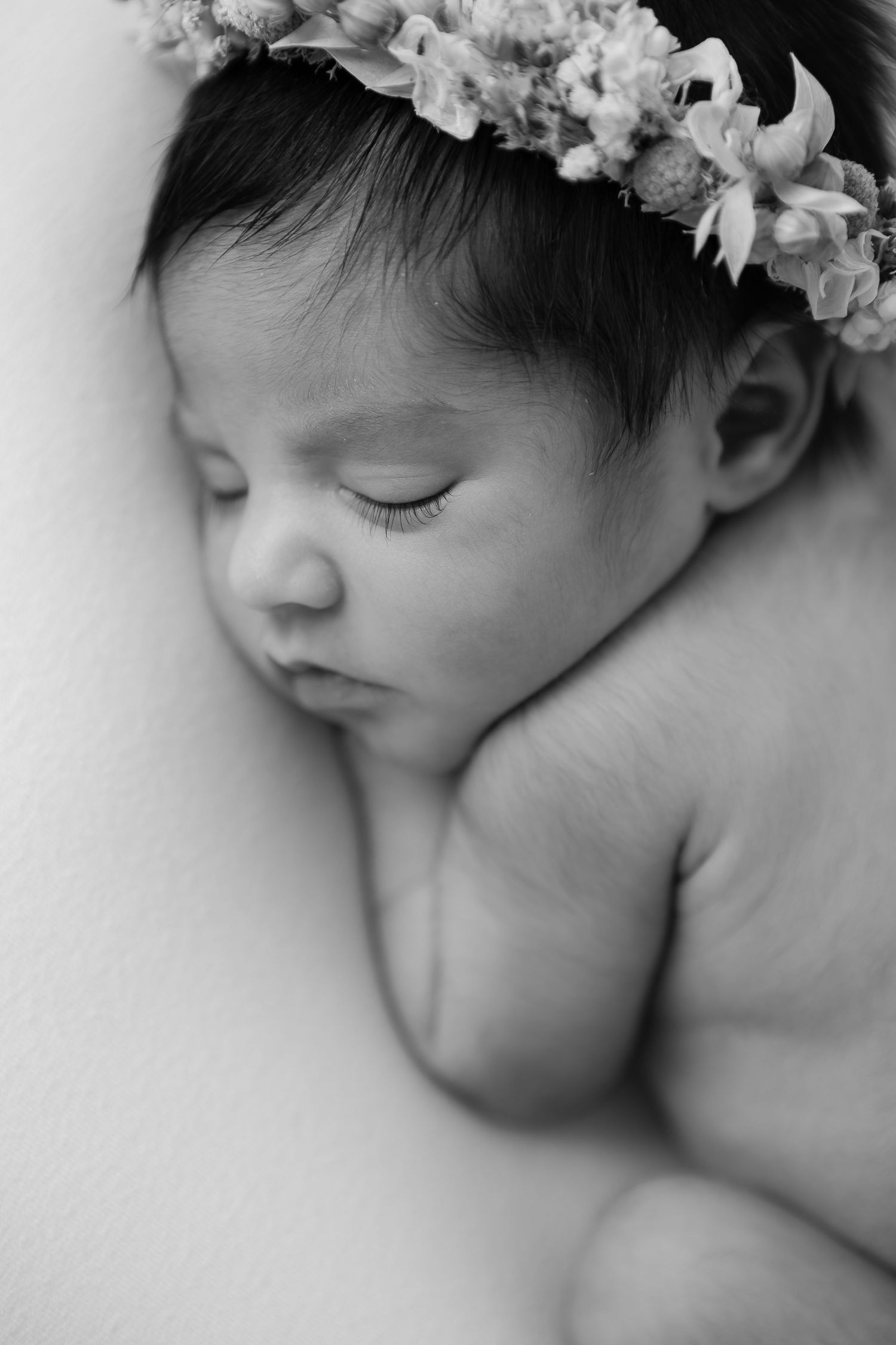 Black and white newborn portrait with delicate floral crown and soft lighting.
