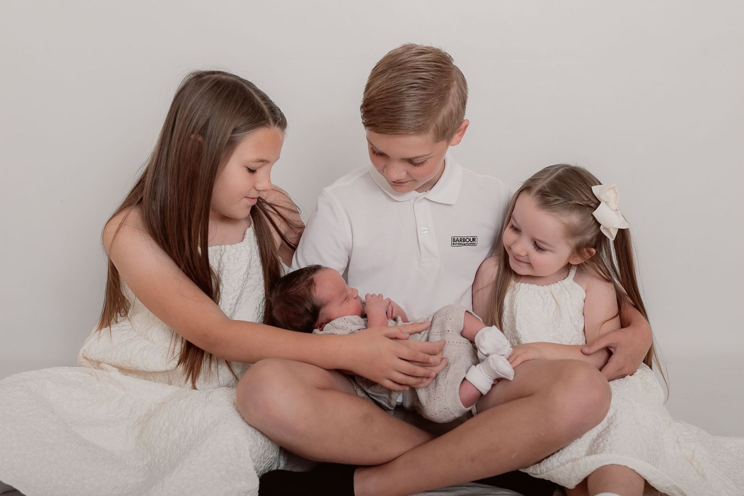 Family members in white clothing sharing tender moments on light grey backdrop.