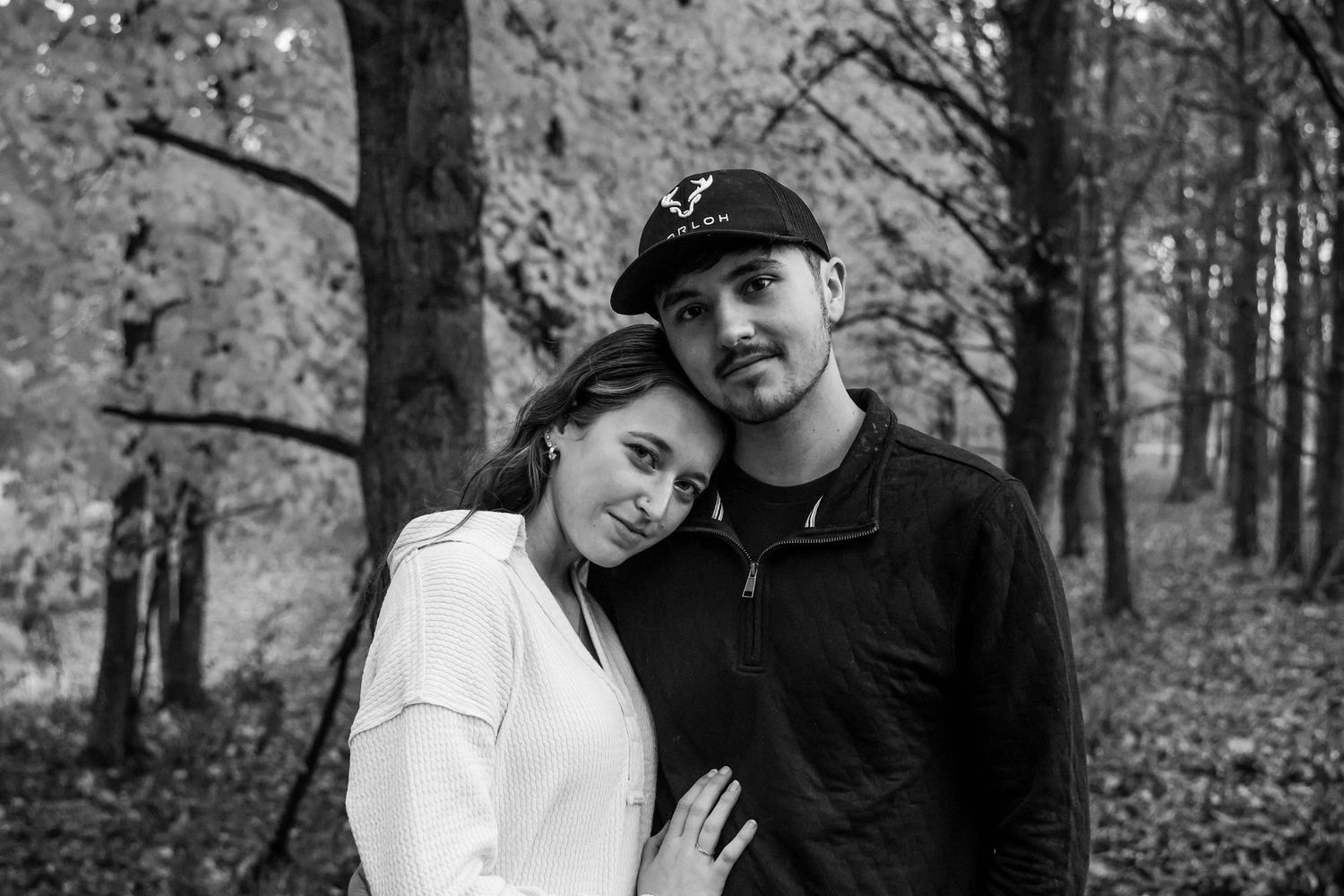 A couple poses together in a wooded setting during an autumn photo session, showing affection in black and white photos.
