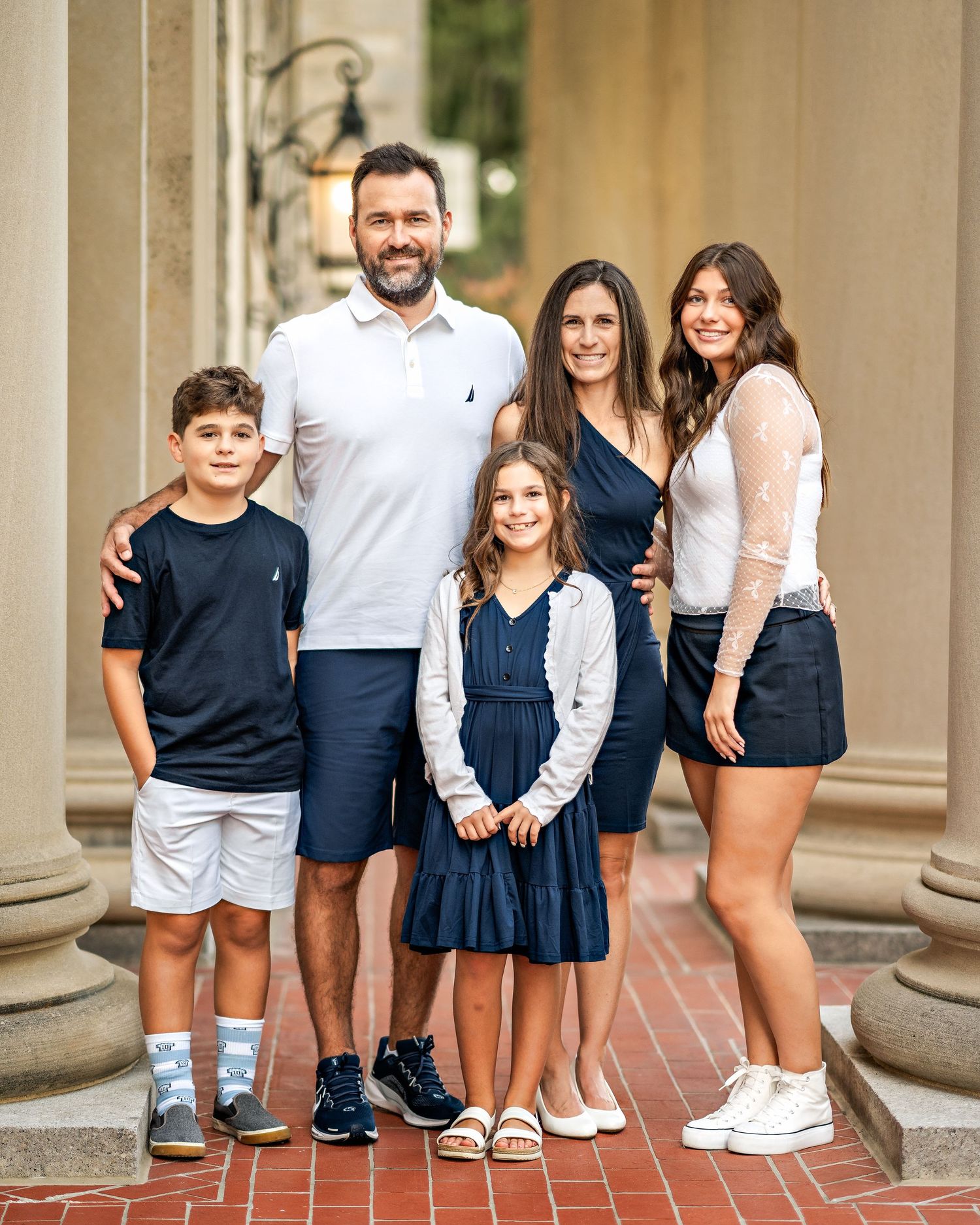 Family poses together in coordinated navy and white outfits against stone pillars during a photo session.