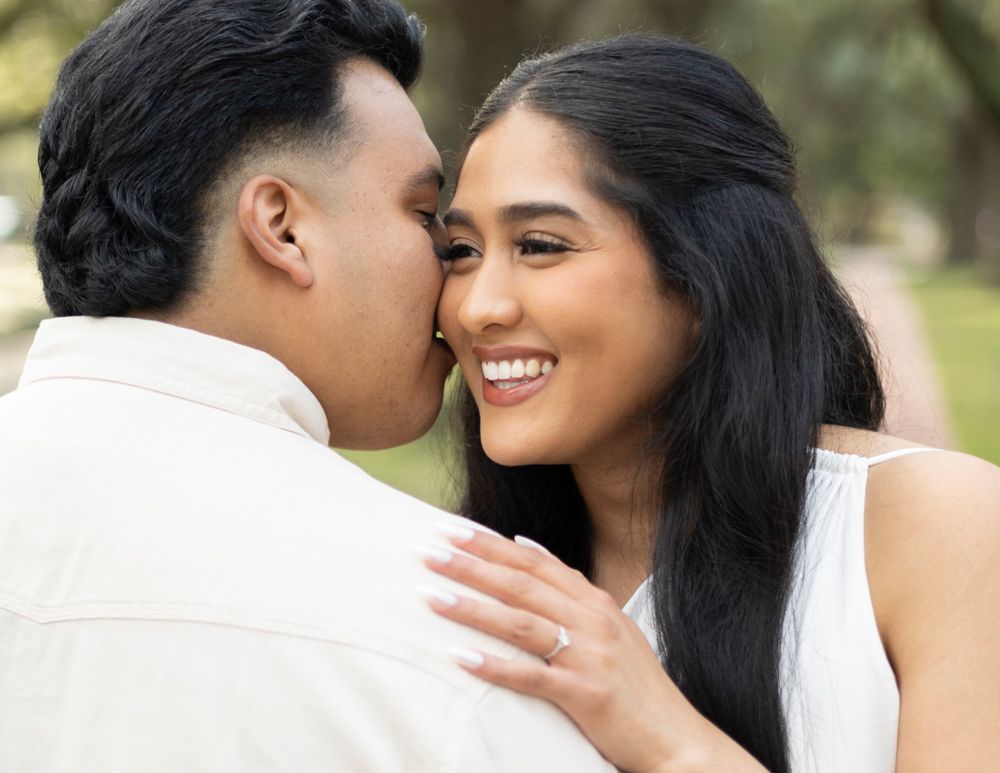 A romantic couple shares a tender moment outdoors as they smile and embrace in white clothing.