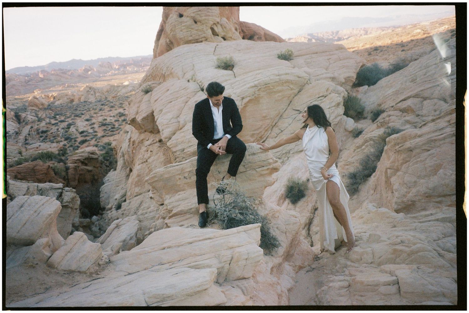 Two people explore the scenic red rock formations at sunset in a desert landscape.