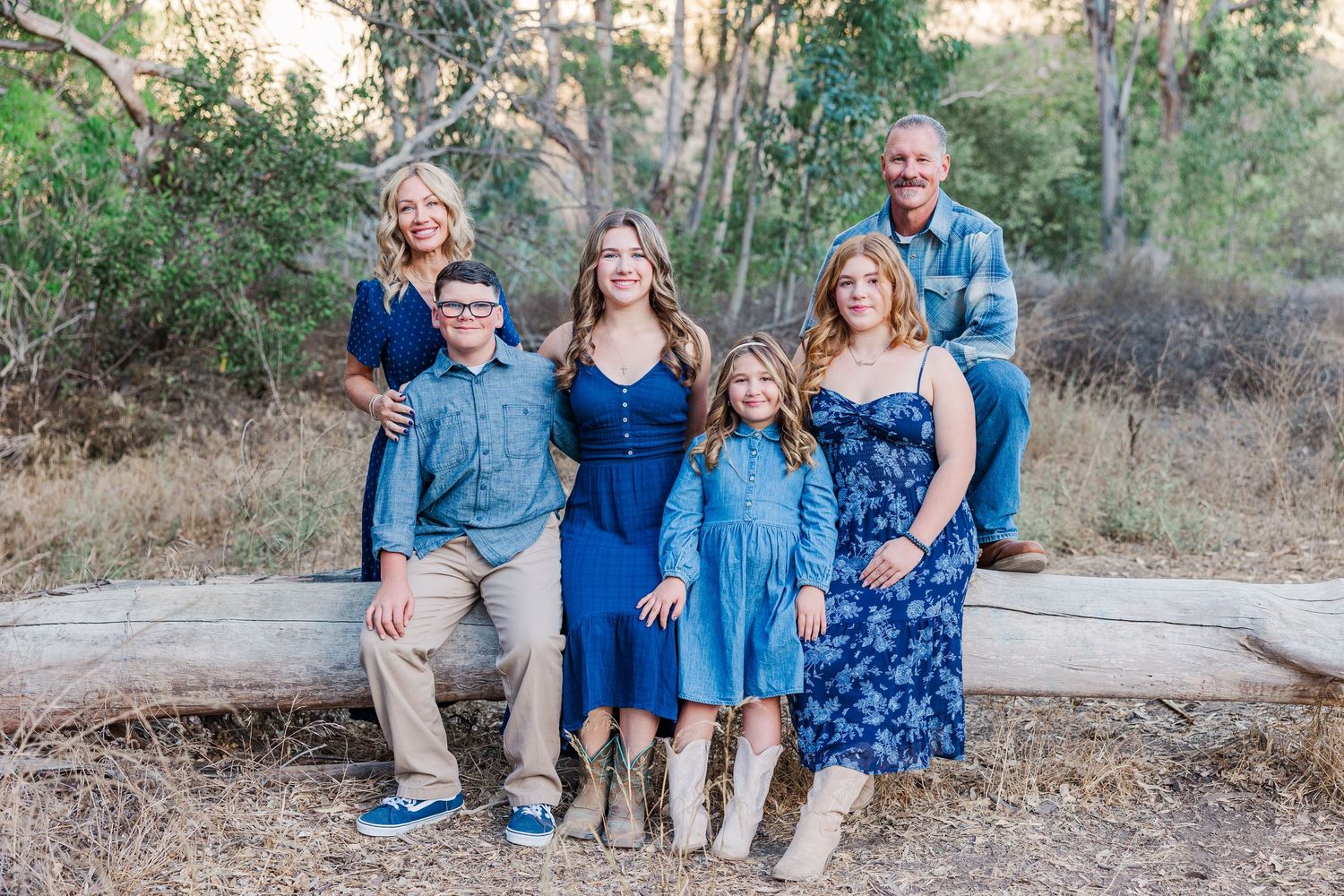 Family wearing coordinated blue outfits poses together outdoors on a nature path during golden hour.