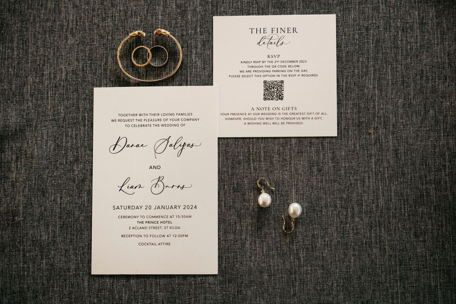 Wedding invitation suite with gold rings and butterfly on dark textured background laid out in flat lay style.