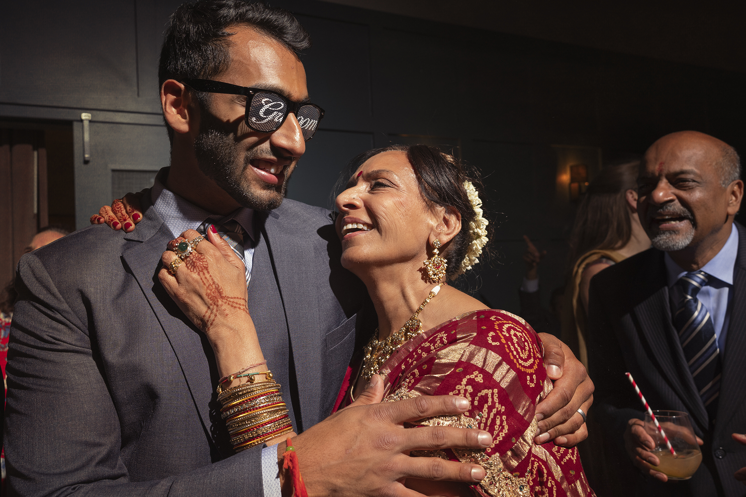 A couple laughs and enjoys a festive indoor celebration while wearing formal attire including a red dress.