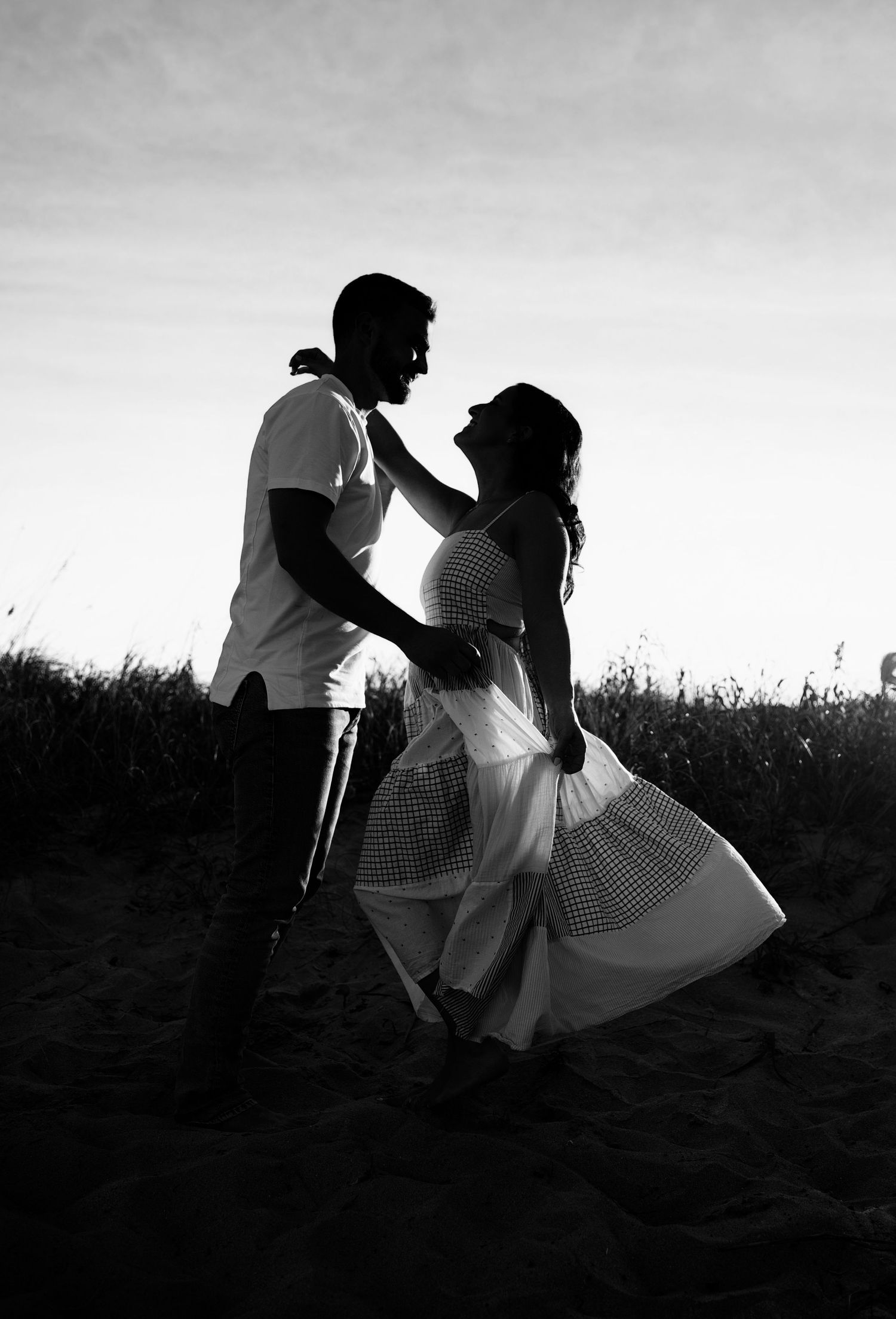 Silhouetted figures dance together in a romantic sequence across a field at sunset creating a dramatic black and white series.