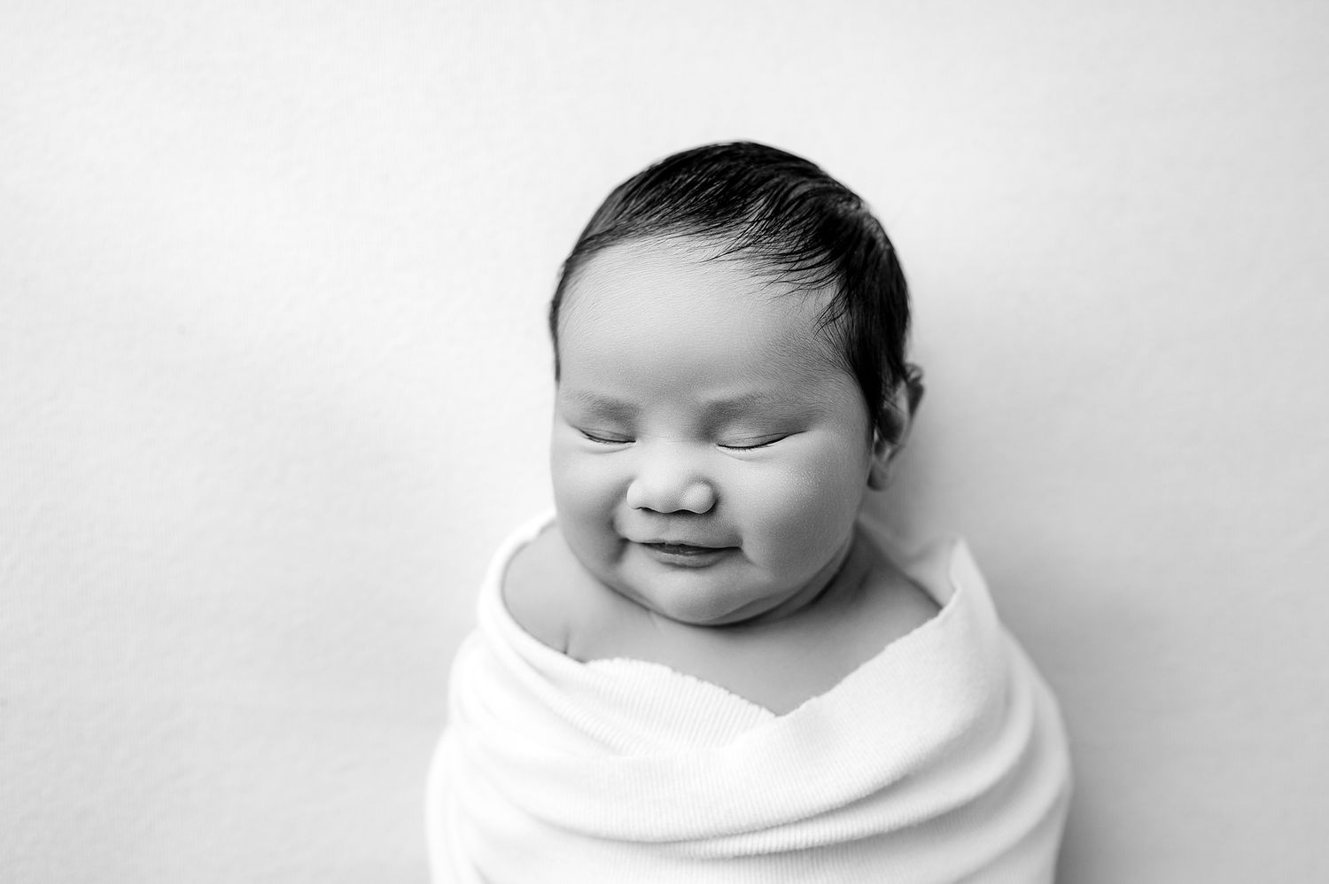 A black and white photo series shows a sleeping newborn baby swaddled in white cloth.