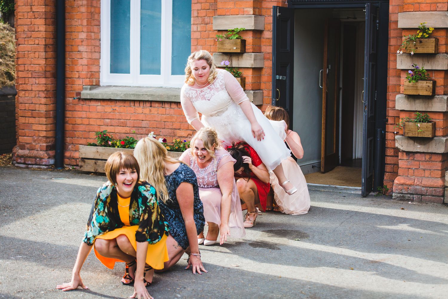 People having fun crawling on the ground in front of a brick building entrance.