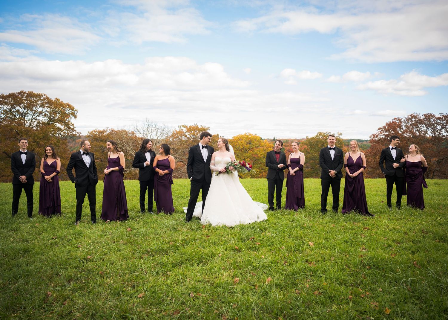 Newlyweds share an intimate moment outdoors with autumn foliage and rustic architecture in background.