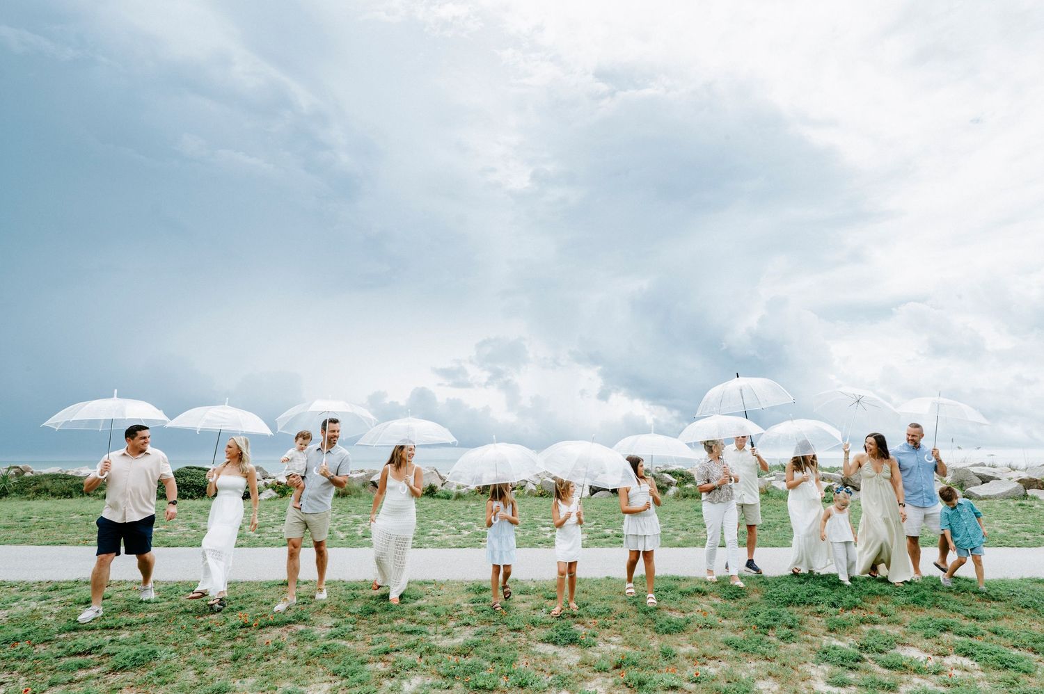 Large group wearing white creates panoramic photo along coastal grassland.