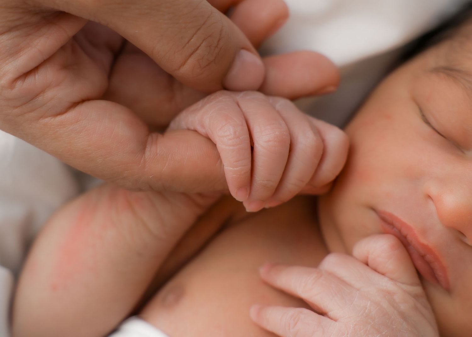 A sleeping newborn baby wrapped in a soft green blanket rests peacefully on white bedding.