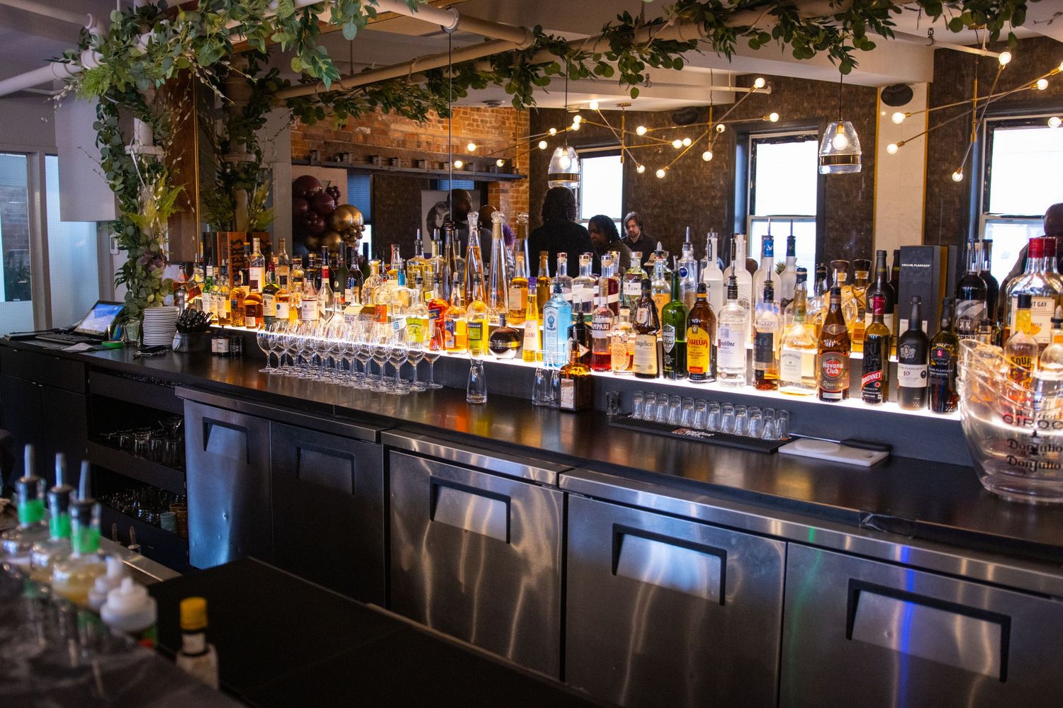 Well-stocked bar with illuminated liquor bottles displayed on wooden shelves in a modern restaurant setting.
