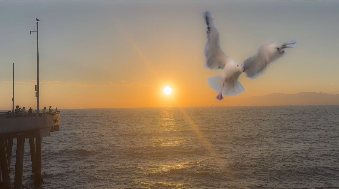 Ocean waves crash along the coast at sunset while seabirds soar through the golden sky over a wooden pier.