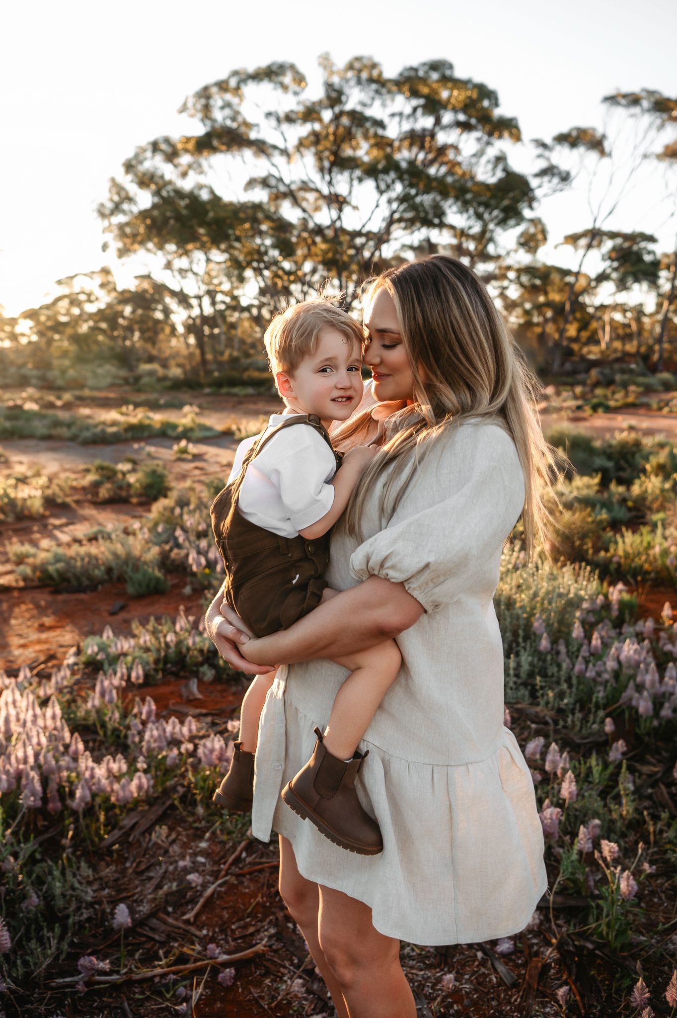 A family shares a joyful moment together outdoors among native Australian bushland at sunset.