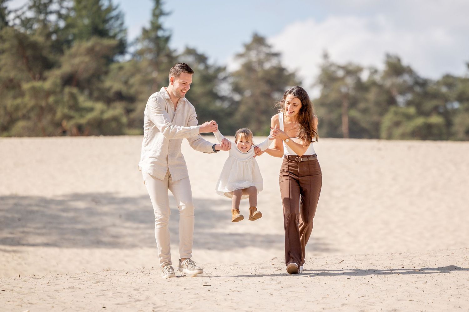 jong gezin op de sahara, waarbij ouders het meisje optillen aan haar armen tussen hen in