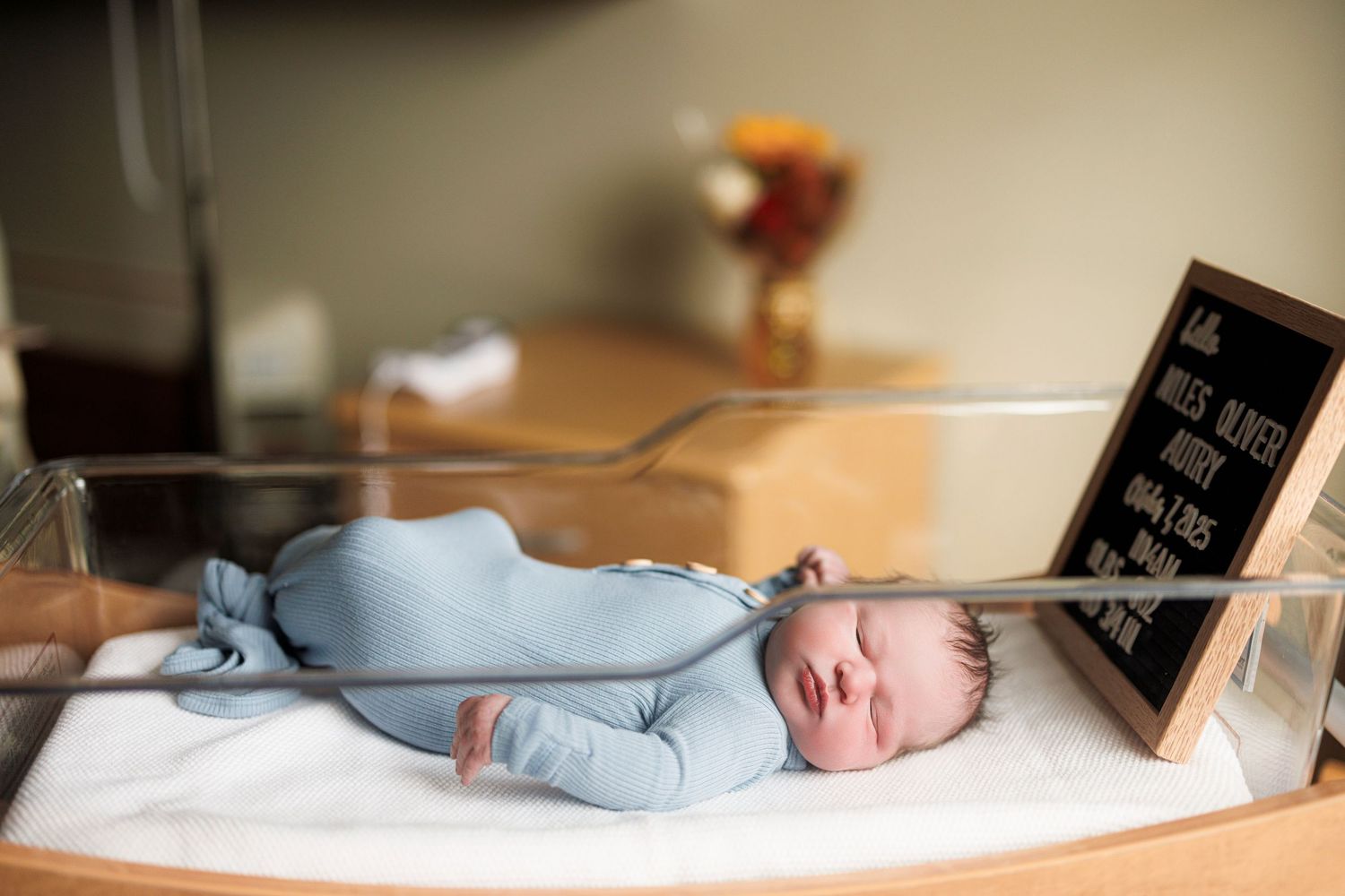 Newborn baby sleeping peacefully in a hospital bassinet with a small name card displayed.
