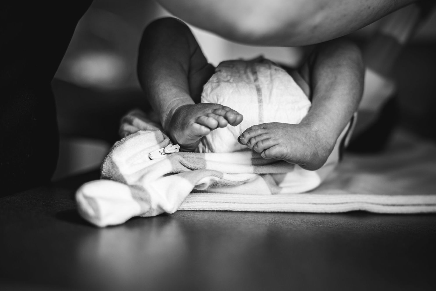Black and white close-up photograph of baby feet and diaper in dim light, as baby lies on changing table.