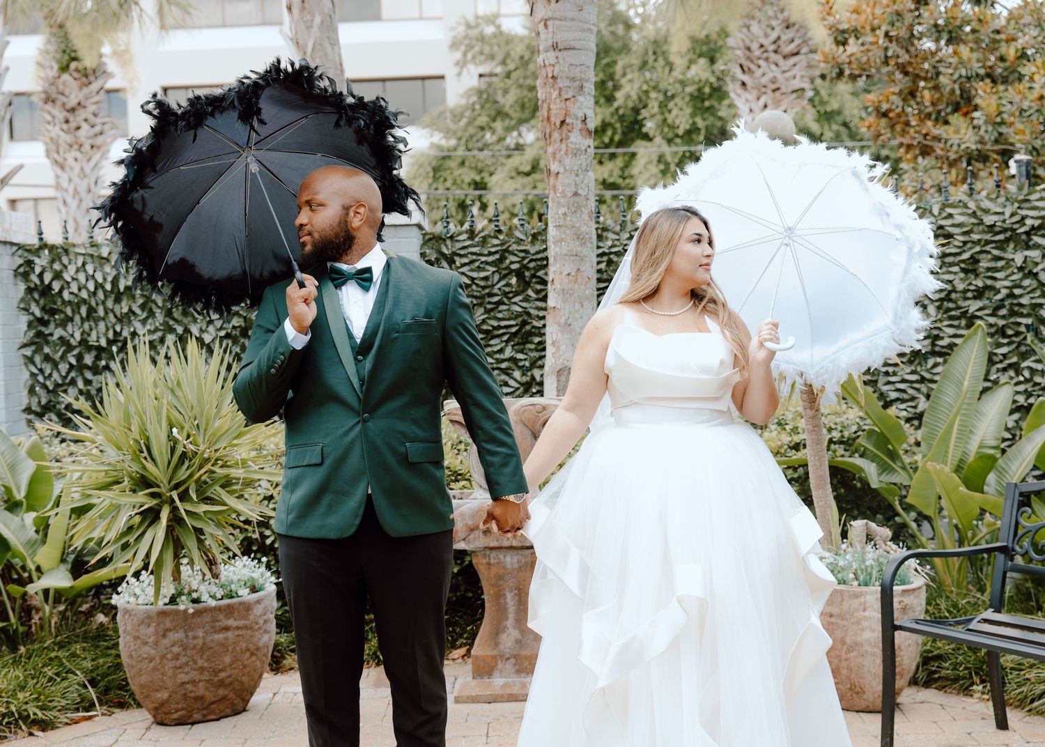 A couple in wedding attire holds black and white parasols while posing in a garden setting.