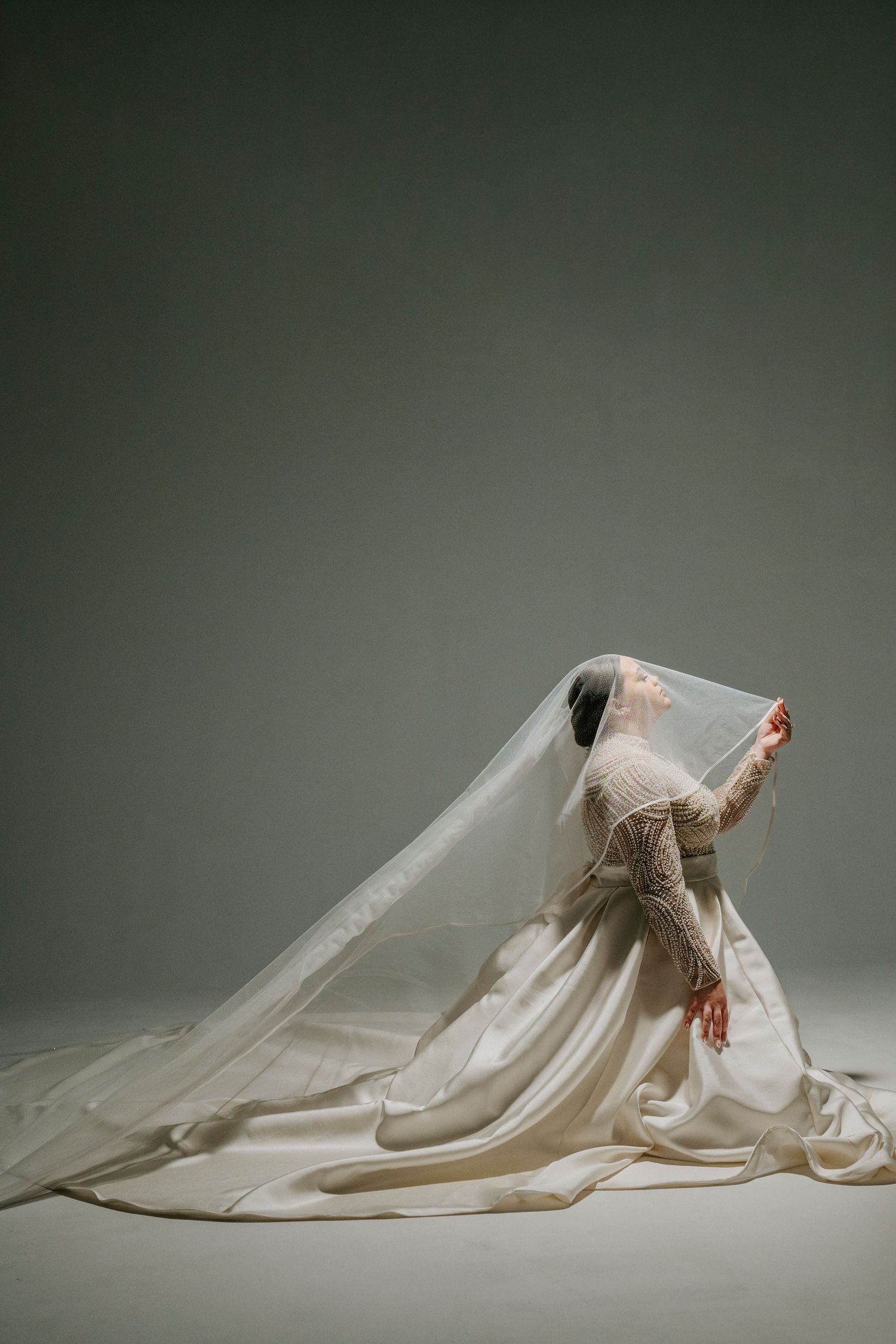 A series of artistic photos showing a person lying under flowing white fabric in different graceful poses against a gray background.