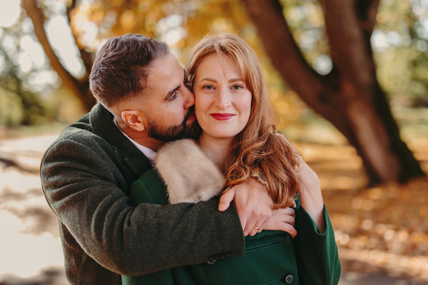 A couple embraces outdoors in a romantic photoshoot under sunlit trees.