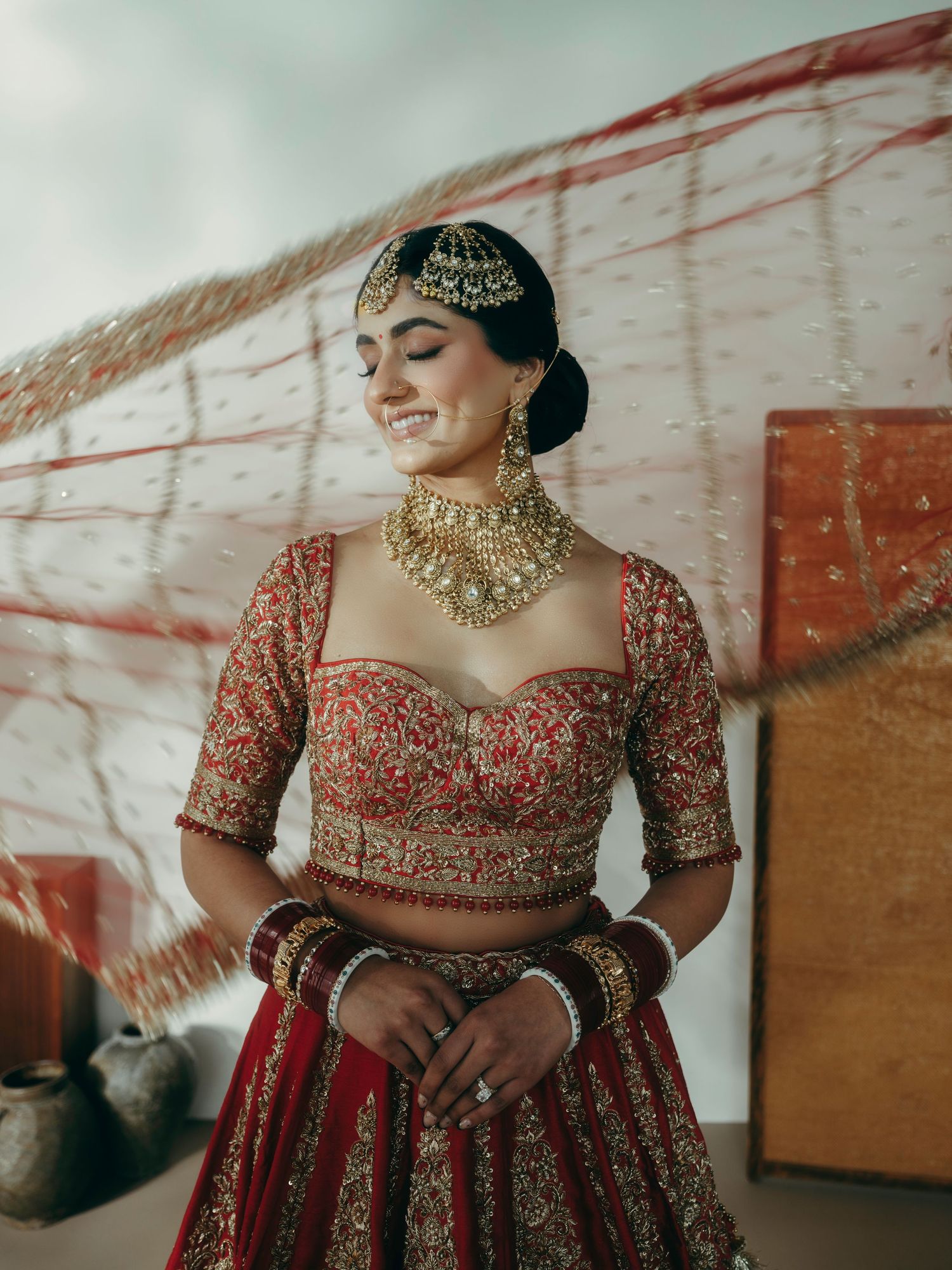 Traditional Indian bridal attire featuring intricate embroidered red lehenga with gold jewelry and detailed beadwork.